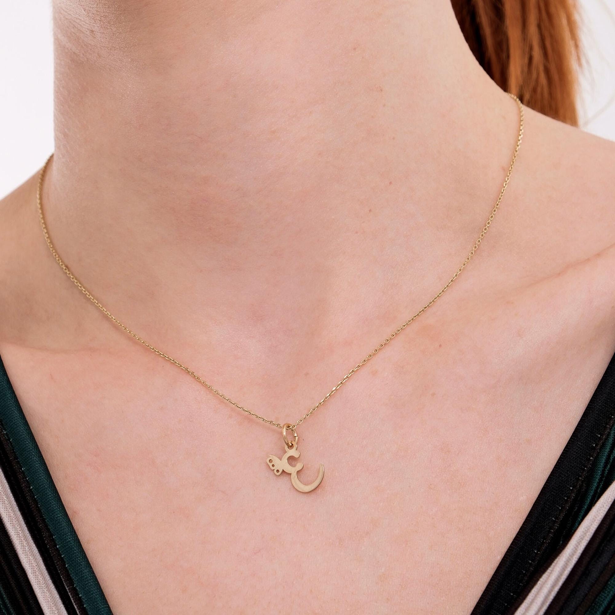 Close-up of a woman's neck wearing a 14K solid gold custom letter necklace with a butterfly charm, featuring an elegant "E" pendant.