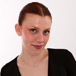 A 14K solid gold cursive initial necklace with the letter "A" and heart charm is laid on soft fabric.