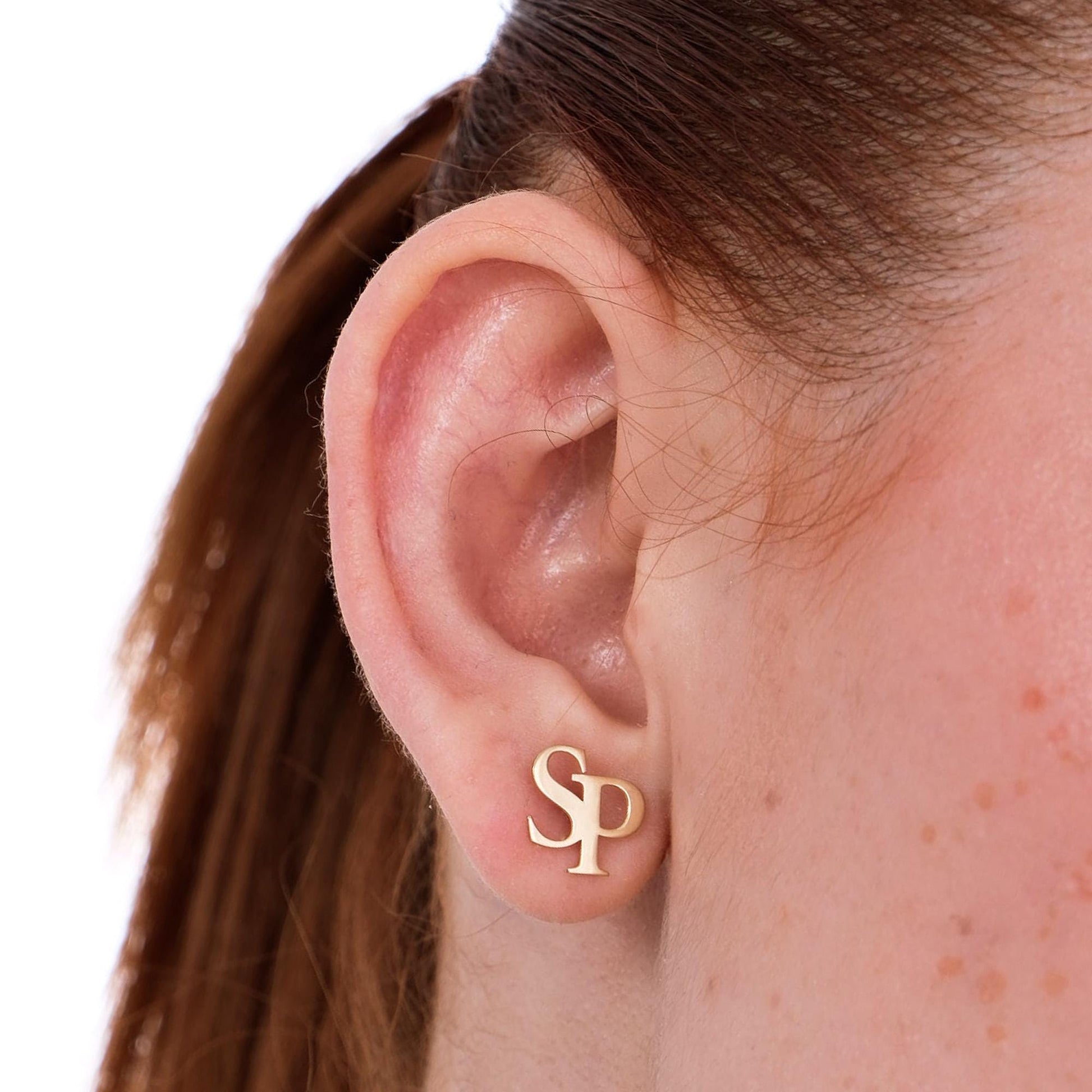 Zoomed-in view of a woman&#39;s ear adorned with 14K solid gold intertwined initial earrings combining the letters “S” and “P”.