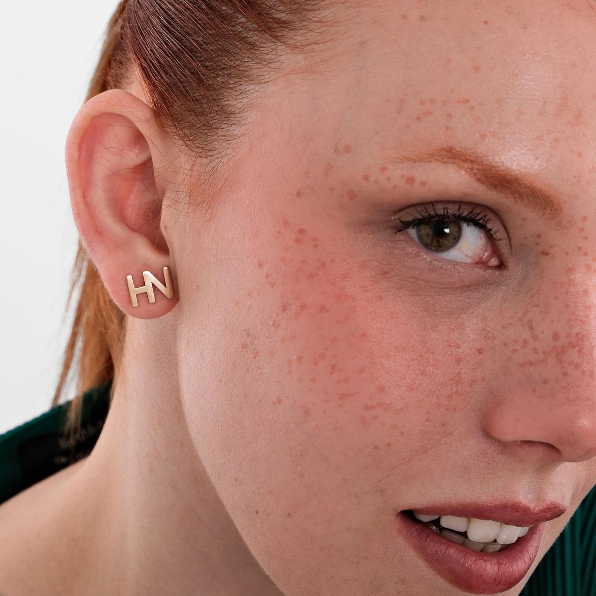 Woman wearing 14K solid gold letter stud earrings with the initials &quot;HN&quot;, shown from the side.