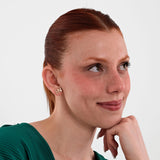 Smiling woman resting her chin on her hand while wearing 14K solid gold "HN" letter stud earrings.