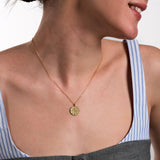 The gold compass pendant on a fine chain, lying flat to display its full intricate pattern.