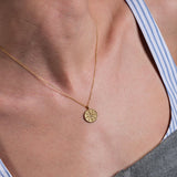 Close-up of a woman's neck wearing a delicate 18K gold vermeil compass necklace on a thin gold chain.