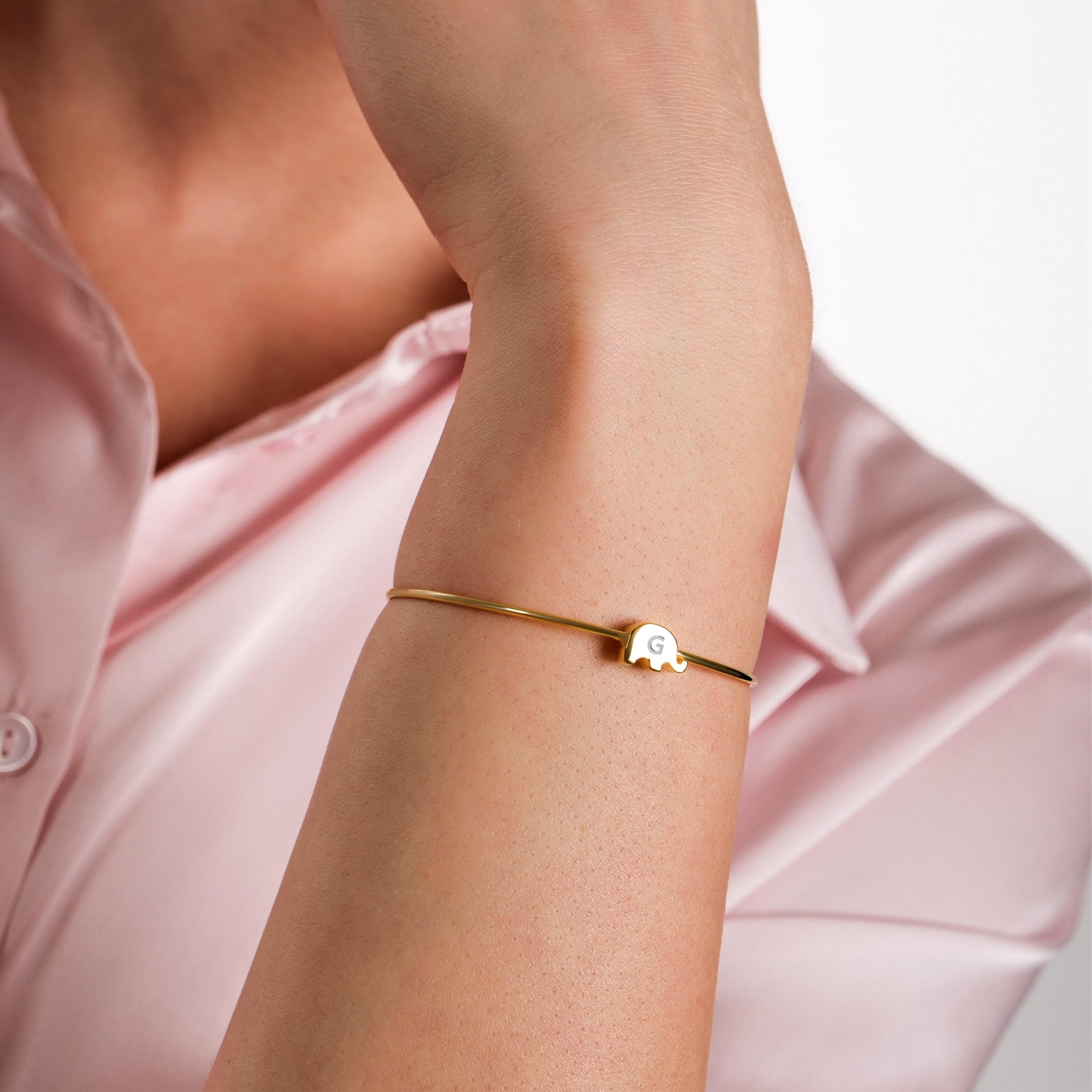 A delicate gold bangle bracelet with an elephant charm on the model’s wrist.