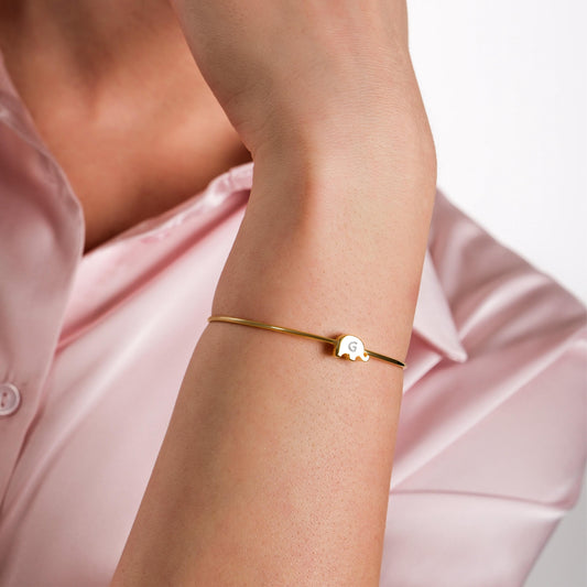 A delicate gold bangle bracelet with an elephant charm on the model’s wrist.