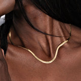 A smooth and elegant 18K gold vermeil personalized herringbone necklace draped around a woman’s neck, with engraved names near the center.