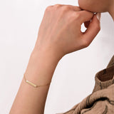 Side view of a woman's wrist adorned with a dainty 14K solid gold engraved bar bracelet featuring Roman numerals.