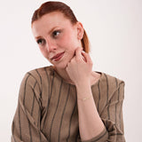 Portrait of a red-haired woman in a striped blouse, subtly displaying a 14K solid gold engraved bar bracelet.