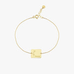 Top view of a 14K solid gold birthflower bracelet featuring a square pendant with floral engraving and personalized name detail.