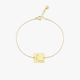 Top view of a 14K solid gold birthflower bracelet featuring a square pendant with floral engraving and personalized name detail.