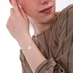 Close-up of a woman’s wrist wearing a 14K solid gold birthflower bracelet engraved with a delicate flower and the name “Rachel”.