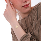 Close-up of a woman’s wrist wearing a 14K solid gold birthflower bracelet engraved with a delicate flower and the name “Rachel”.