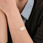 Portrait of a woman in a denim shirt and dark cardigan, showcasing a 14K solid gold custom engraved bracelet.