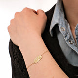 Close-up of a woman's wrist wearing a 14K solid gold custom engraved bracelet with the initials "SHB" on an oval plate.