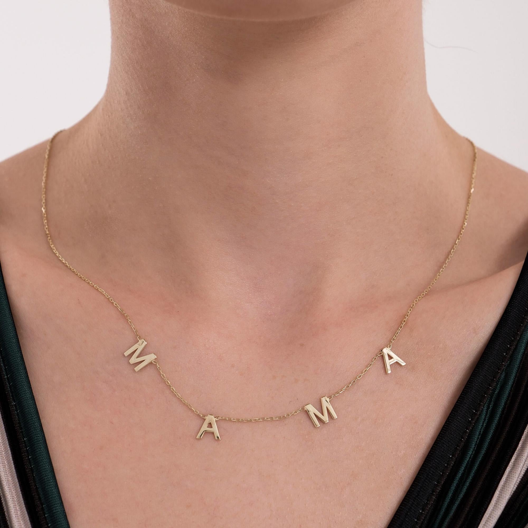 Front view of a 14K solid gold mama necklace resting on a woman’s collarbone, each letter spaced evenly along a delicate chain.