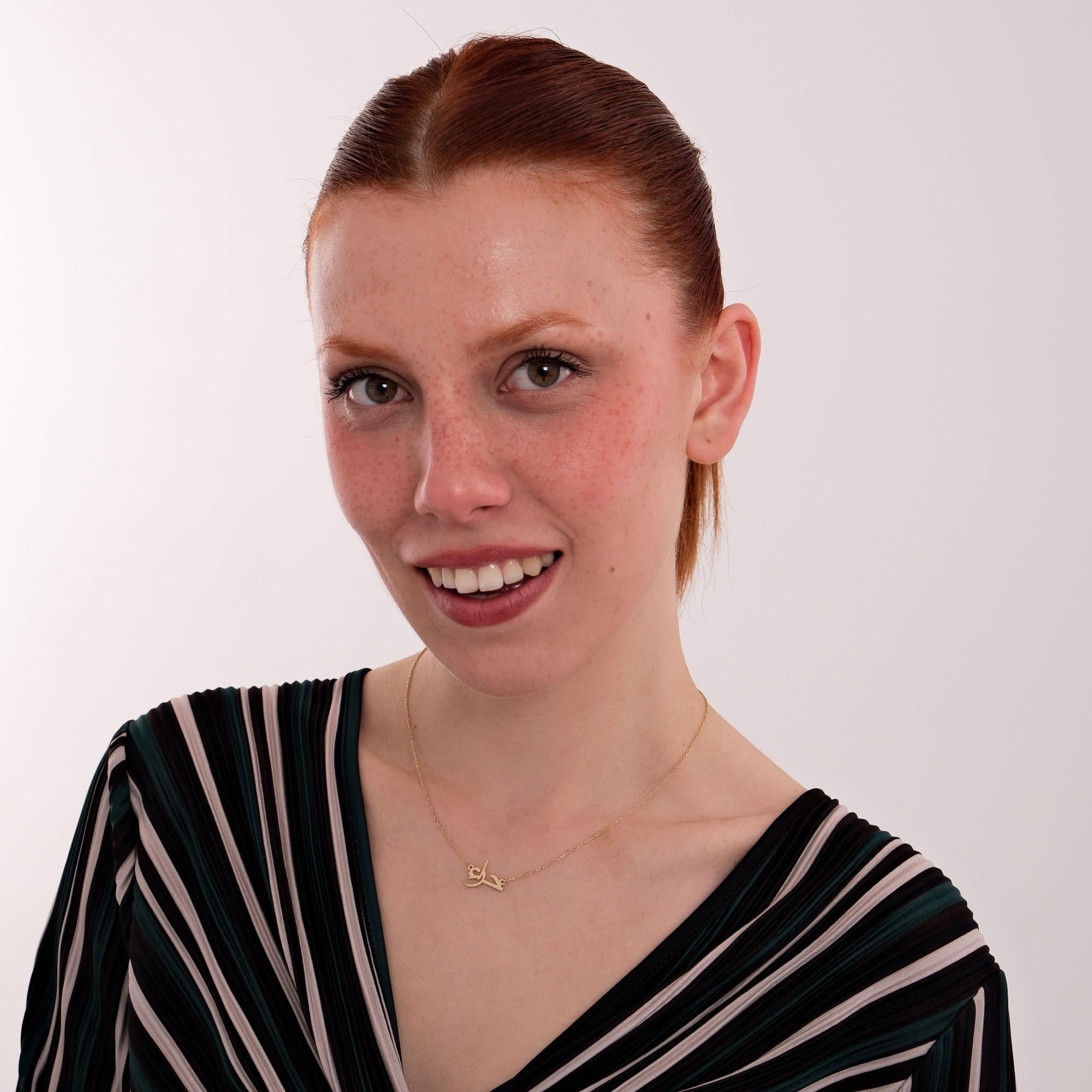 Portrait of a red-haired woman smiling at the camera, styled in a striped dress and accessorized with a 14K solid gold Arabic name necklace that adds a refined touch.