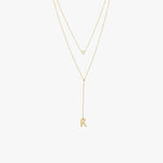 Flat lay of a 14K solid gold pearl lariat necklace featuring a single pearl and a 'K' charm, styled with two fine gold chains.