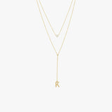 Flat lay of a 14K solid gold pearl lariat necklace featuring a single pearl and a 'K' charm, styled with two fine gold chains.