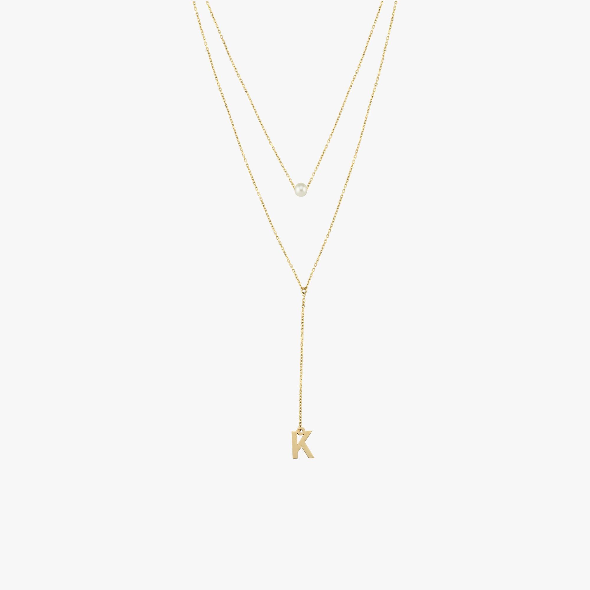 Flat lay of a 14K solid gold pearl lariat necklace featuring a single pearl and a 'K' charm, styled with two fine gold chains.