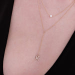 Zoomed-in view of a woman's chest wearing a 14K solid gold pearl lariat necklace, showing the elegant gold chain, pearl detail, and letter charm.