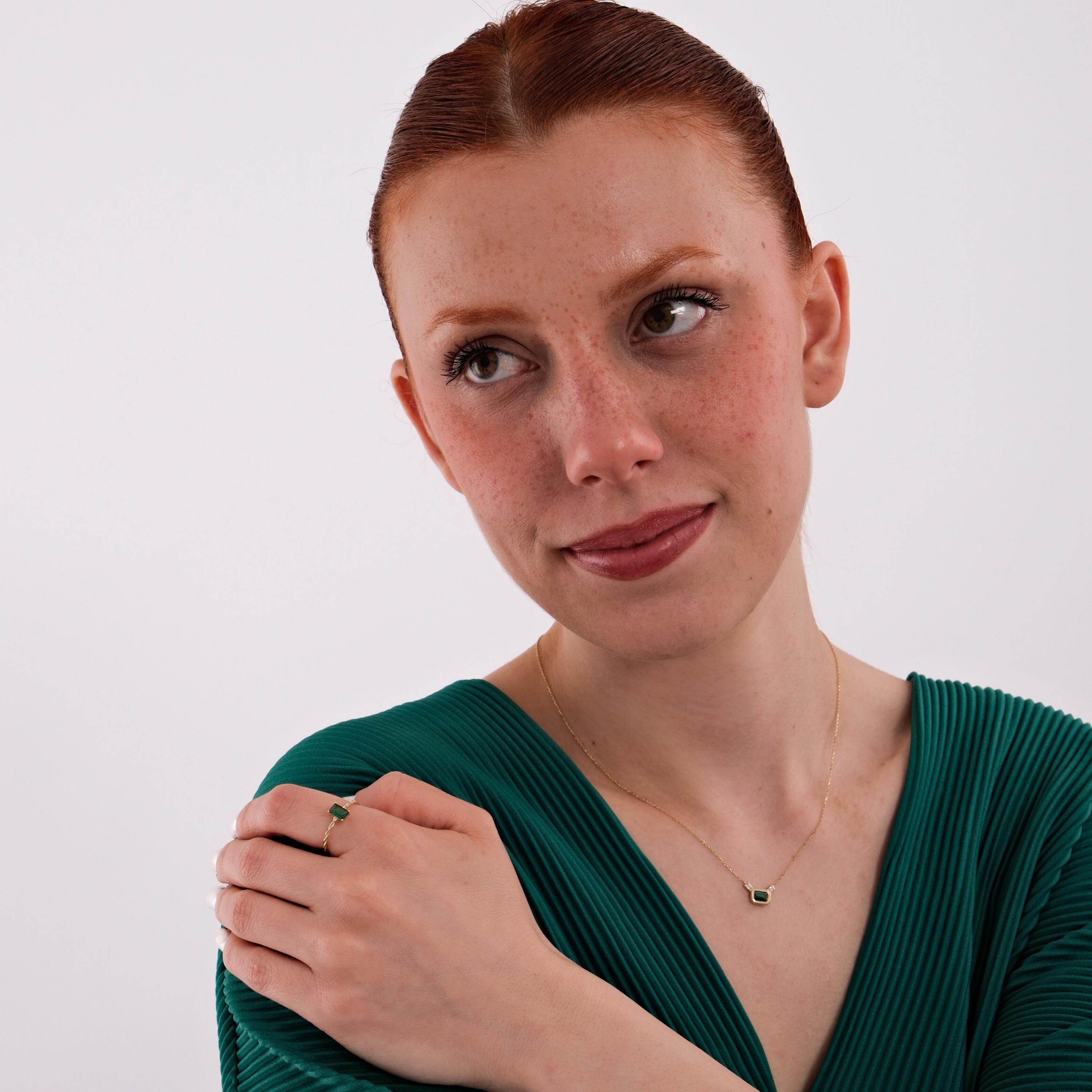 A full shot of the model posing with both the 14K Solid Gold Emerald Cut Ring and the matching necklace, styled with a green pleated dress.