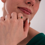 The model rests her hand near her chin, showcasing the 14K Solid Gold Emerald Cut Ring with a twisted band and deep green stone.
