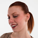 With a gentle smile, the model poses in a ribbed beige top while wearing 14K Solid Gold Initial Stud Earrings.