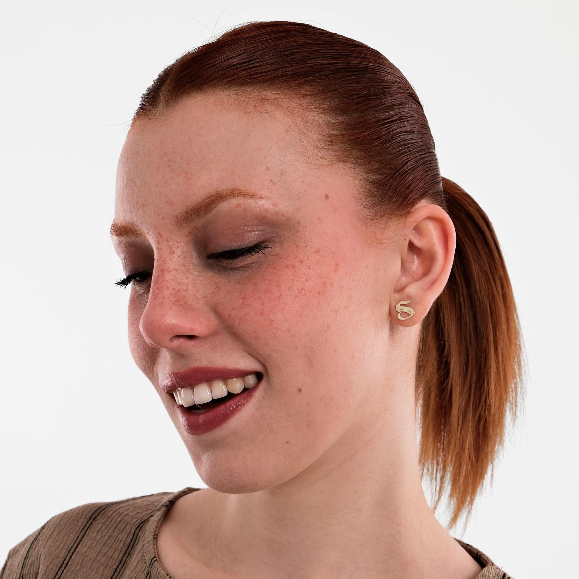 With a gentle smile, the model poses in a ribbed beige top while wearing 14K Solid Gold Initial Stud Earrings.