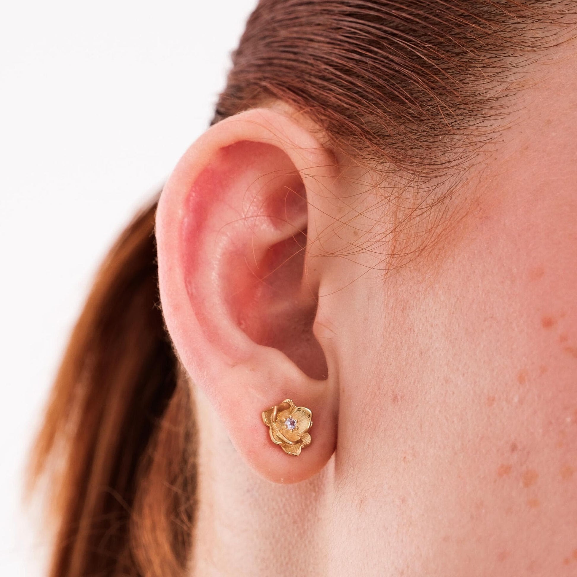 Close-up of 18K gold vermeil birthflower earrings resting on a soft beige fabric, showing their intricate floral design.