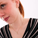 Hand holding a 14K solid gold custom letter necklace with butterfly charm, featuring the letter "E" on a shimmering gold chain.