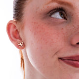 Woman smiling softly while showcasing a 14K solid gold intertwined initial earring with the letters “S” and “P”.