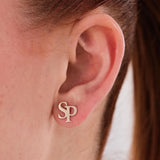 Close-up of a woman's ear wearing 14K solid gold intertwined initial earrings featuring the letters “S” and “P”.