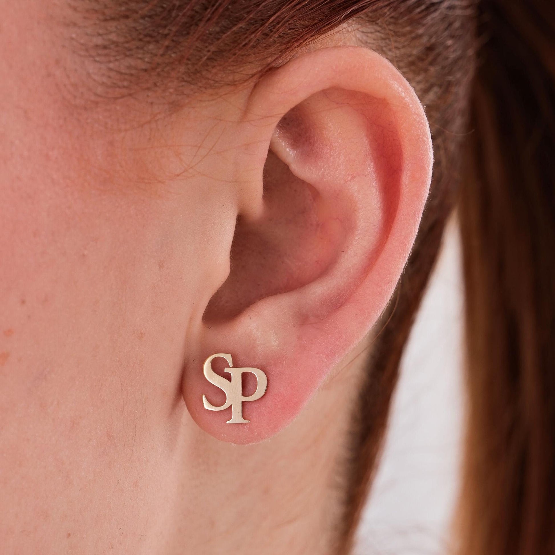 Close-up of a woman&#39;s ear wearing 14K solid gold intertwined initial earrings featuring the letters “S” and “P”.