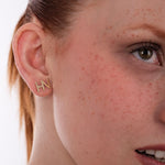 Zoomed-in view of 14K solid gold letter stud earrings in the shape of "HN", worn on a woman's ear.