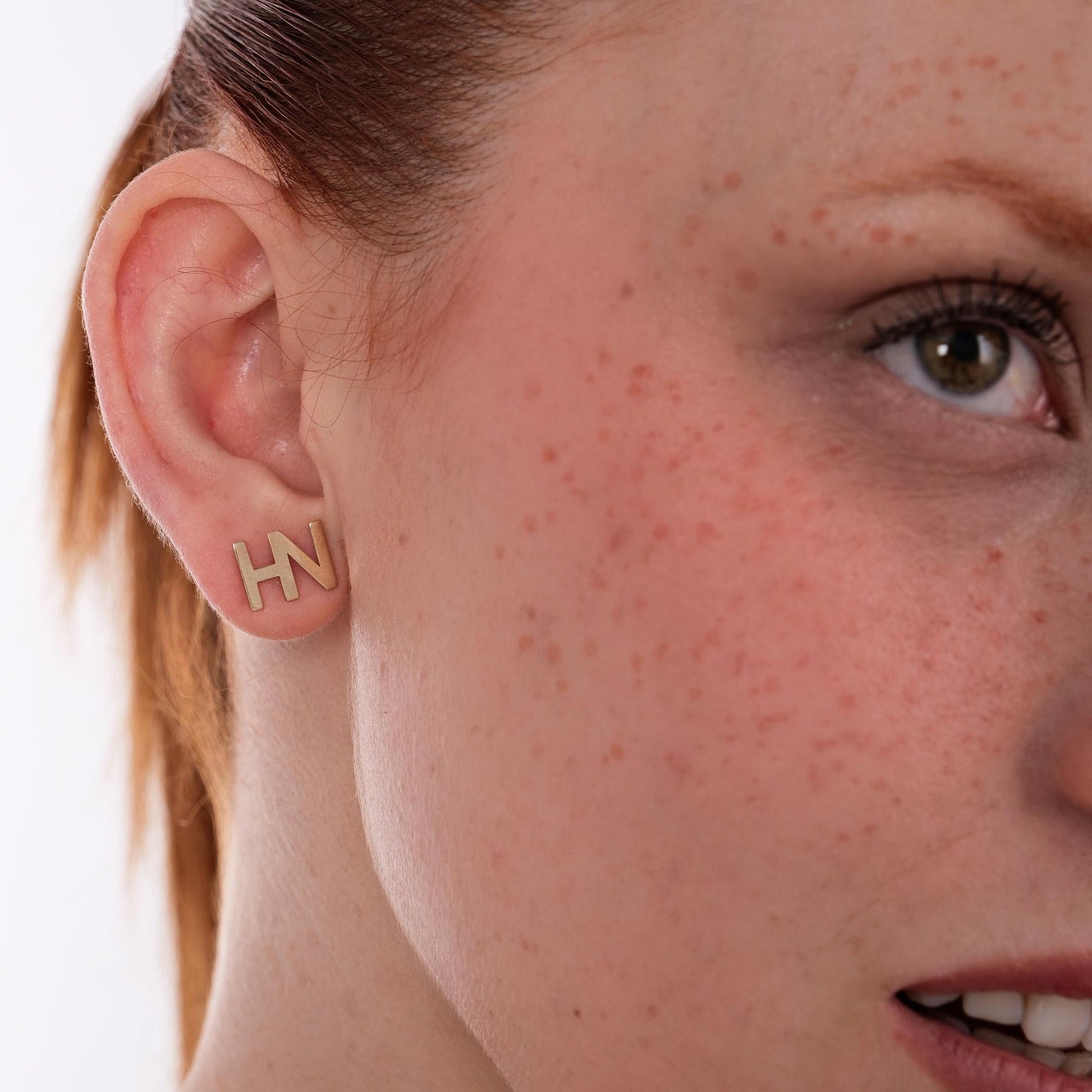 Zoomed-in view of 14K solid gold letter stud earrings in the shape of &quot;HN&quot;, worn on a woman&#39;s ear.