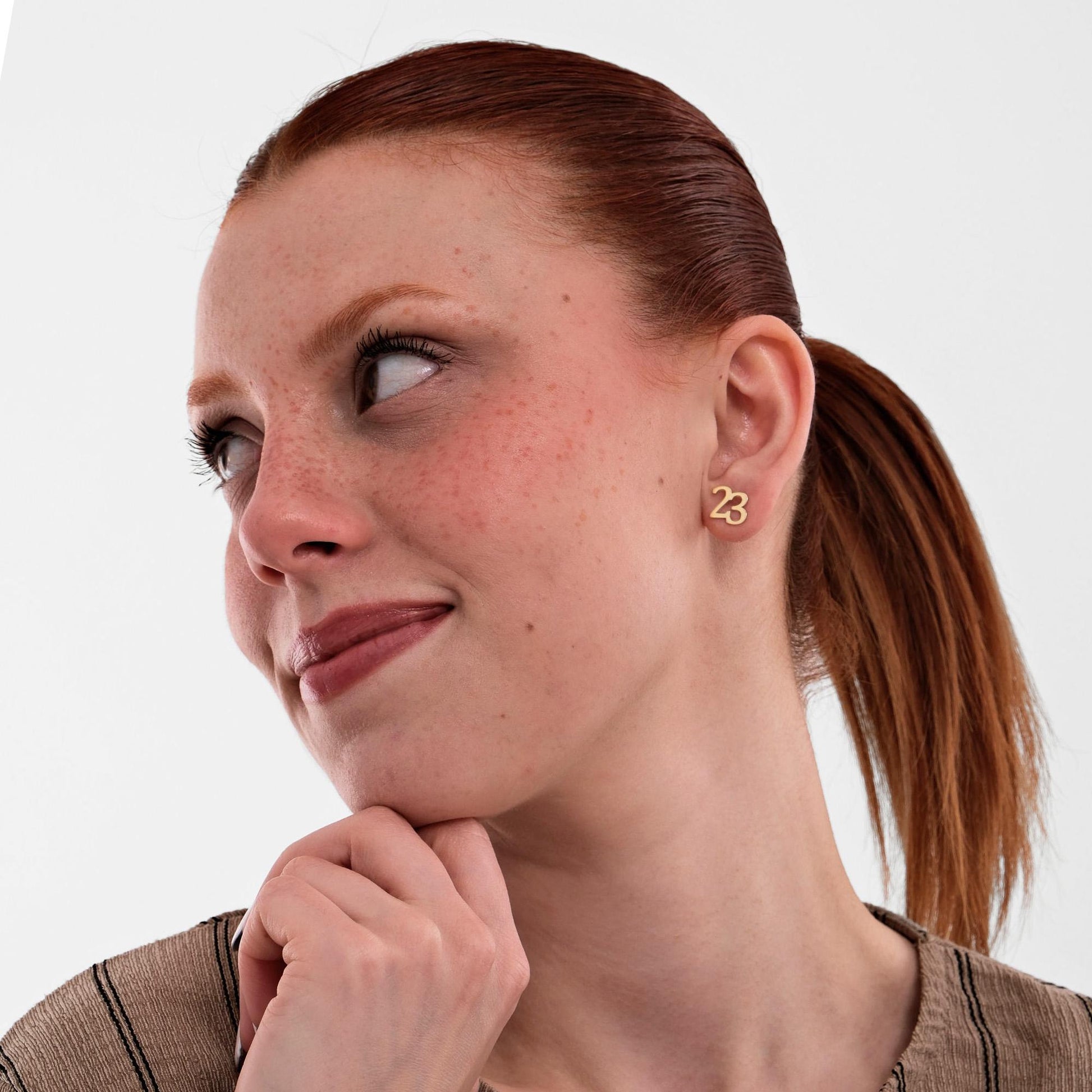 Minimal and stylish 14K solid gold number stud earrings shaped as 23, seen on a smiling woman looking sideways.