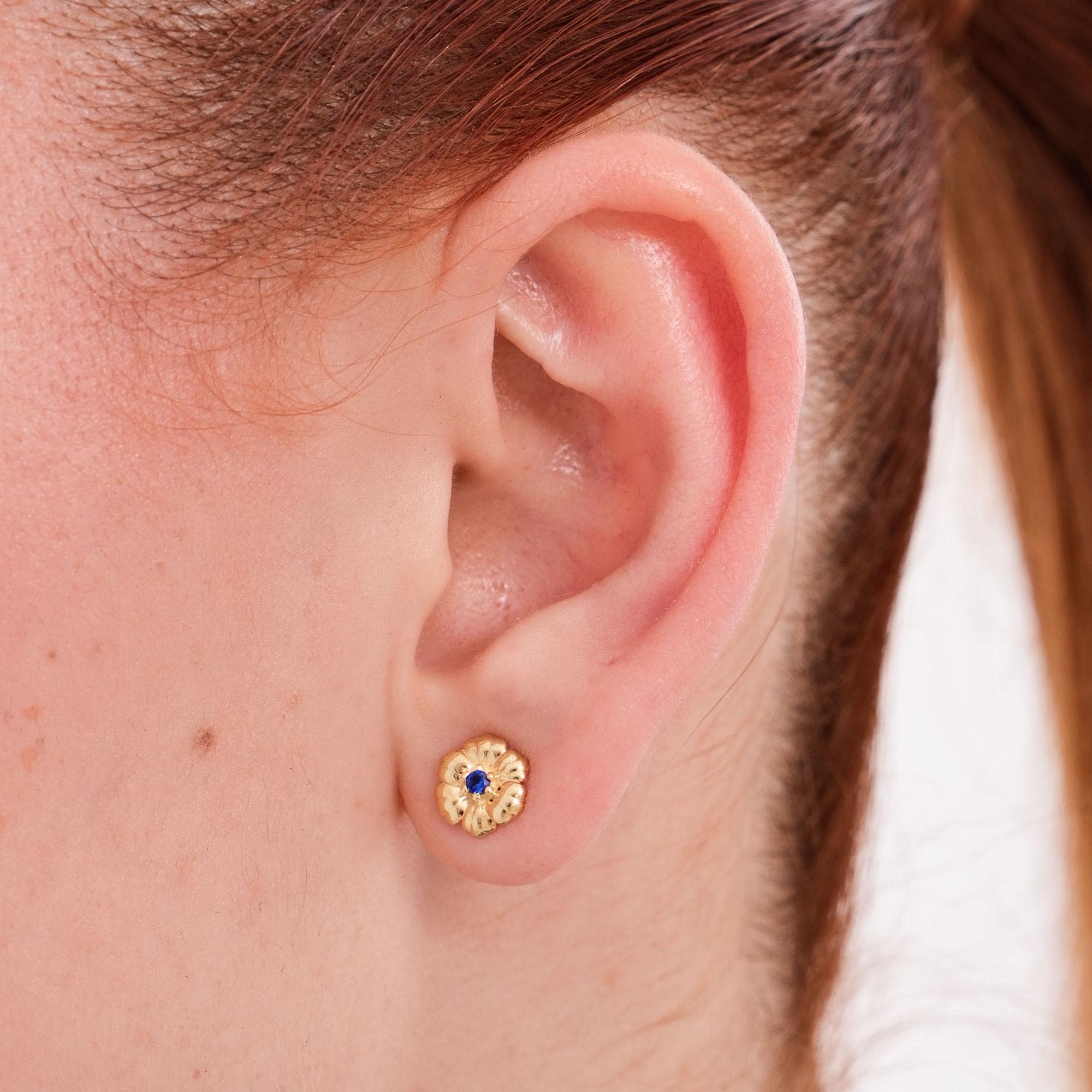 Close-up of 18K gold vermeil birthstone earrings featuring a textured floral design with a deep blue sapphire center.