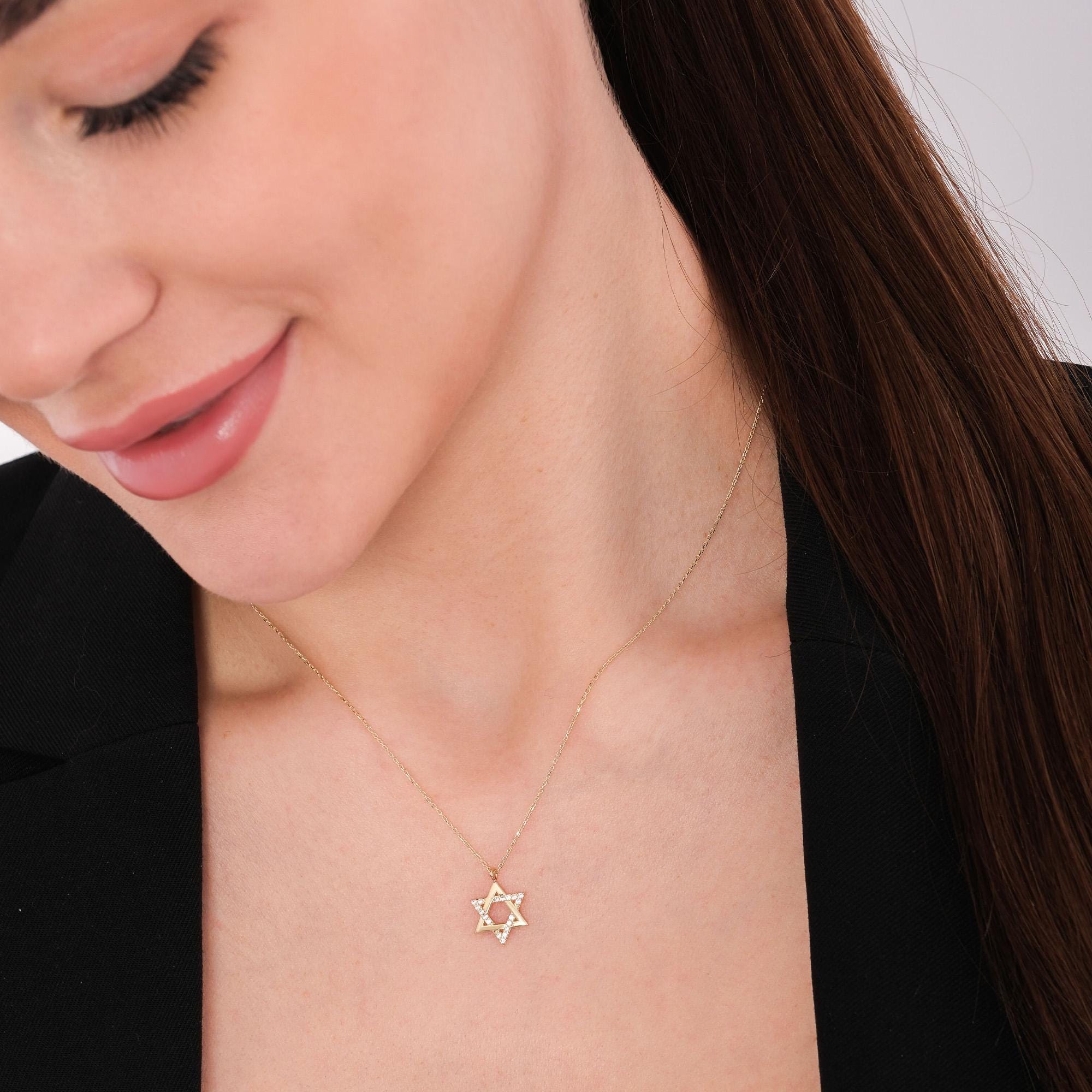 Woman looking down while wearing a 14K solid gold Star of David necklace with a polished geometric pendant and diamond accents.