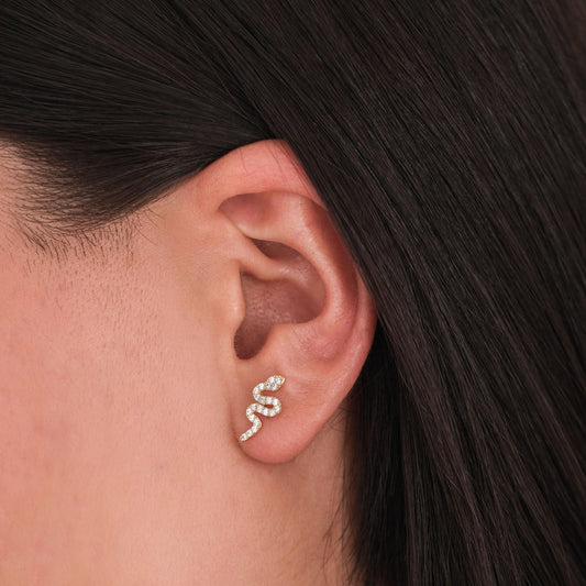 Close-up of a 14K solid gold snake stud earring with pavé diamonds on a woman&#39;s earlobe.