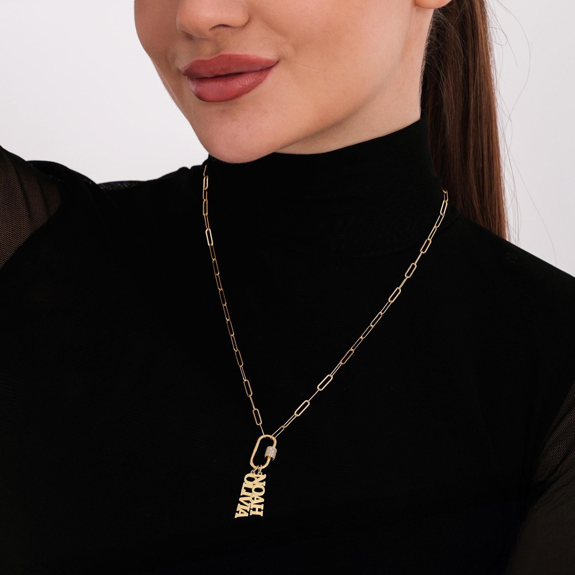 Smiling woman modeling a 18K gold vermeil carabiner charm necklace with “NOAH” and “OLIVIA” name charms, highlighting both the jewelry and elegant styling.