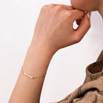 Profile view of a woman's wrist featuring a delicate 14K solid gold custom name bracelet engraved with "ISABEL" against a light background.
