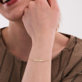 Close-up of a woman wearing a 14K solid gold custom name bracelet engraved with "ISABEL", with her hand near her face, smiling.
