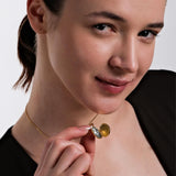 A smiling woman gently opens her 18K Gold Vermeil Photo Locket Necklace to reveal a photo inside.