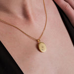 Close-up of a woman wearing an oval-shaped 18K Gold Vermeil Photo Locket Necklace engraved with a compass star and the letter “N”.
