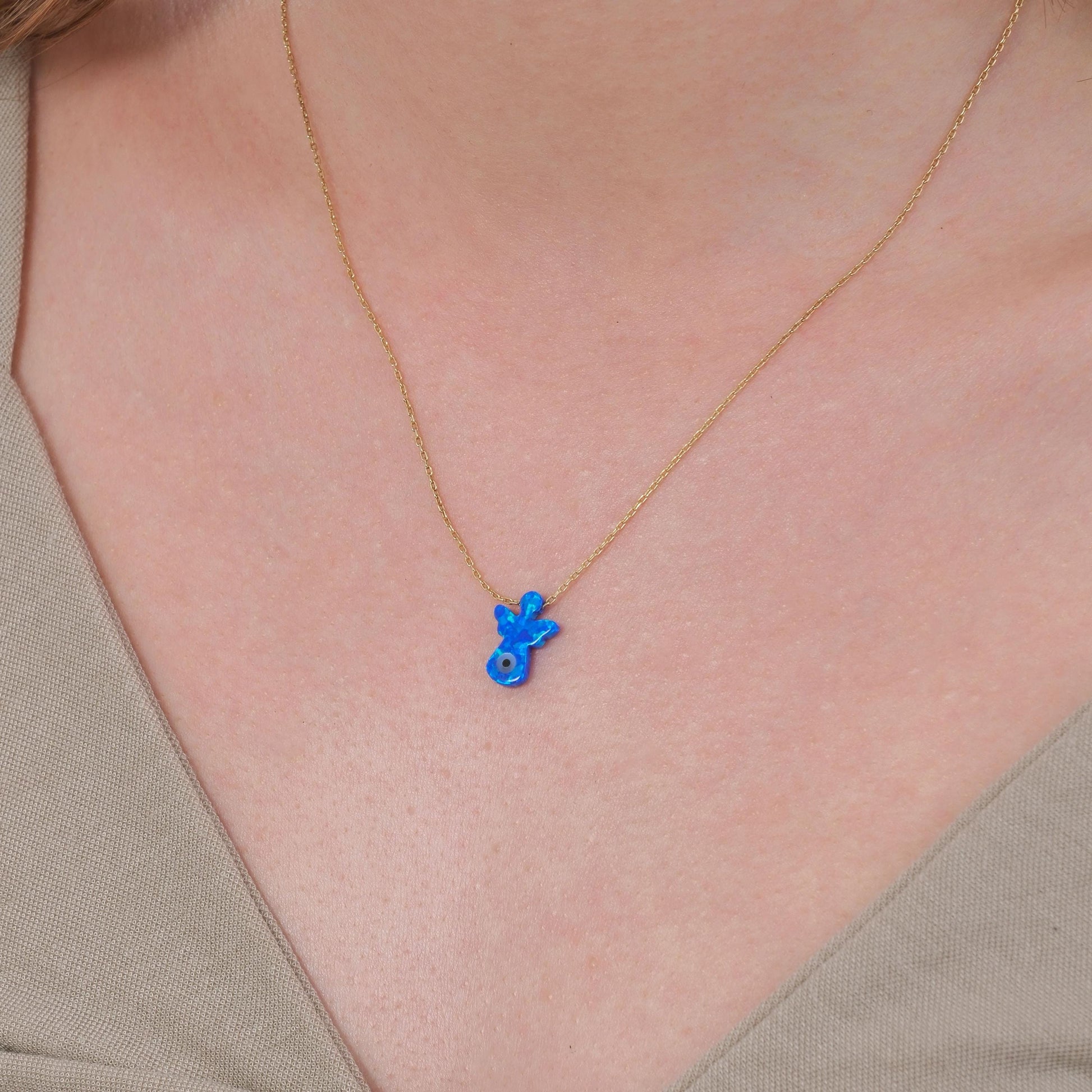 Close-up of a woman’s neck wearing a 14K solid gold lucky symbol necklace with a blue angel pendant and evil eye detail.