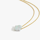 Flat lay of the 14K solid gold opal Hamsa hand necklace with a shimmering white opal pendant on a delicate chain.
