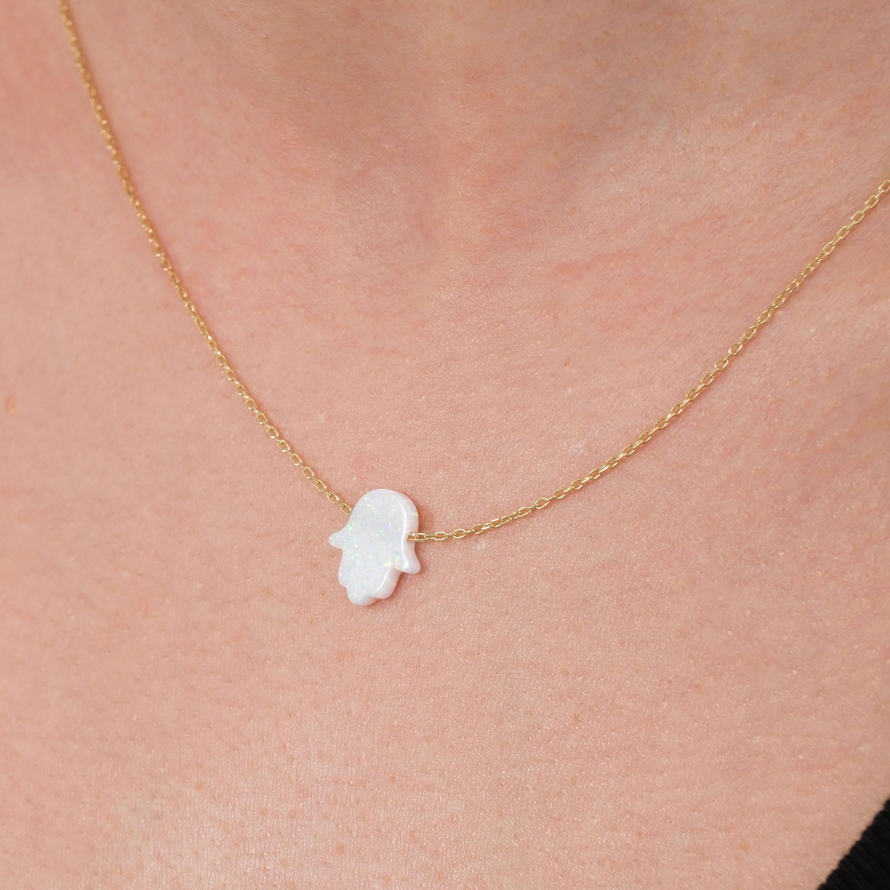 Close-up of a woman wearing a 14K solid gold opal Hamsa hand necklace featuring a subtle iridescent charm.