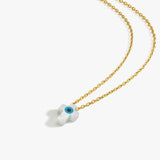 Flat lay of the 14K solid gold cross evil eye necklace with a white cross-shaped pendant and a vivid blue eye detail.