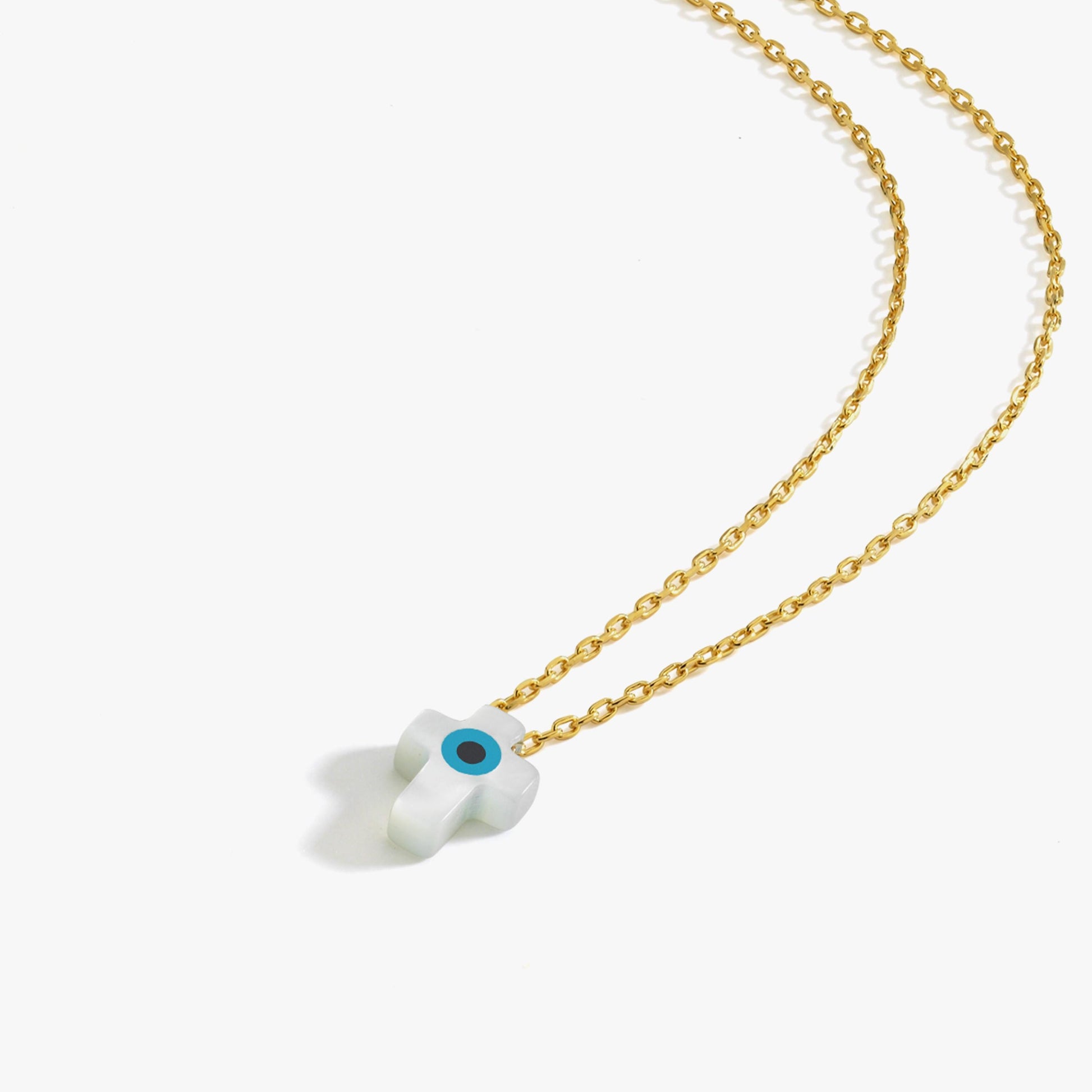 Flat lay of the 14K solid gold cross evil eye necklace with a white cross-shaped pendant and a vivid blue eye detail.