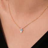 Angled shot of the 14K solid gold cross evil eye necklace resting gently on the skin, emphasizing the pendant's shine.
